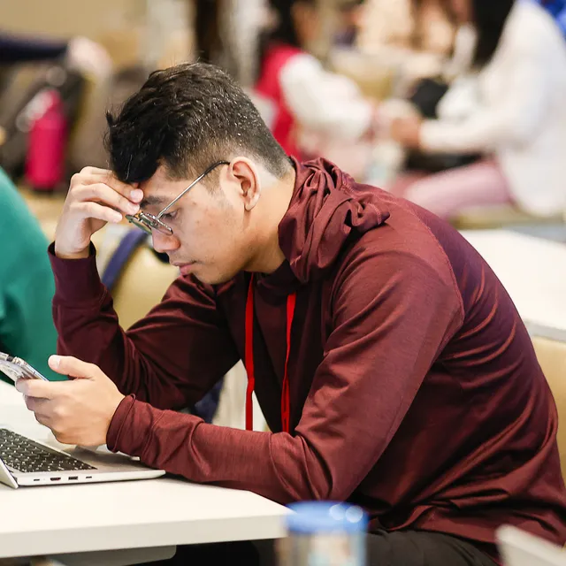 Josh Macaraig at a laptop, wearing glasses and a dark red hoodie.